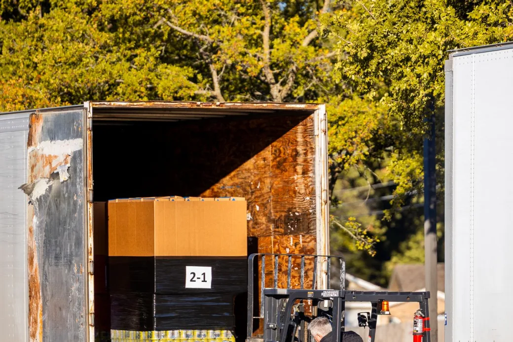 Forklift loading a pallet of boxes into the back of an open semi-trailer