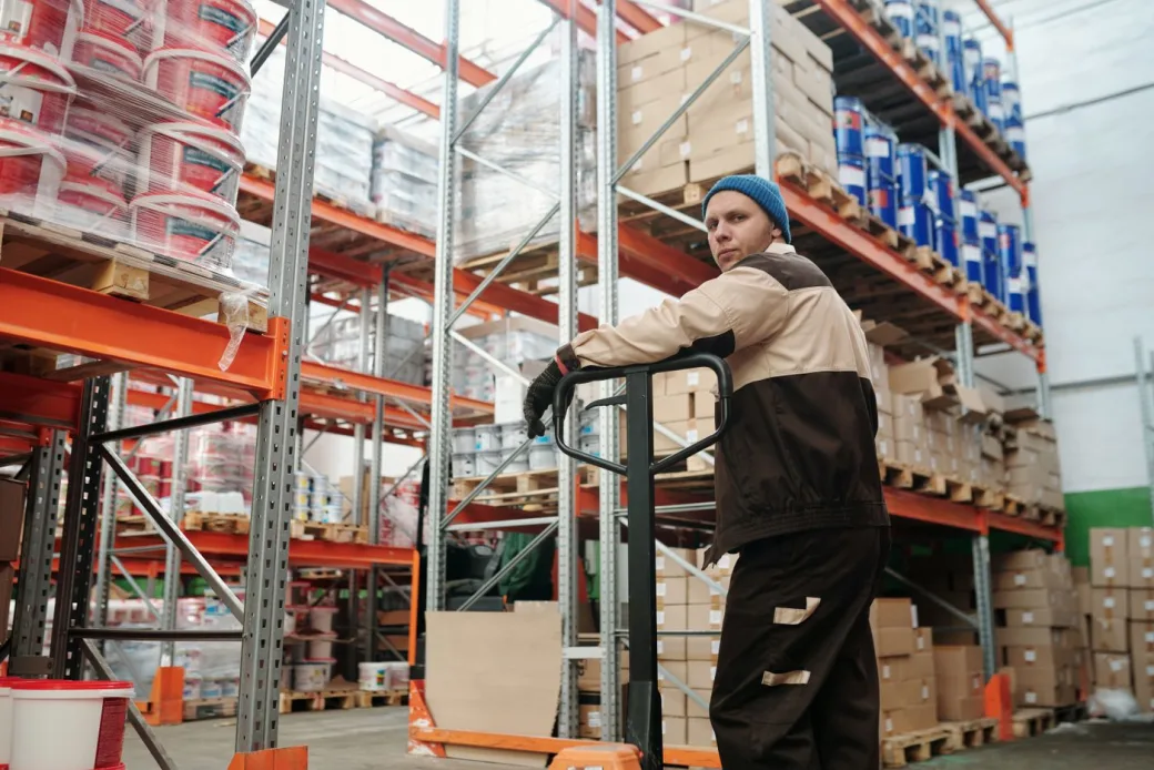Warehouse worker moving a wrapped pallet of goods with a pallet jack