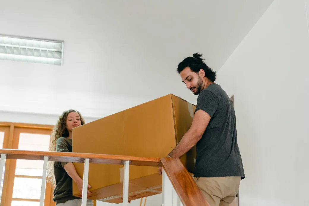 Two people carrying a large piece of furniture up a staircase in an apartment building