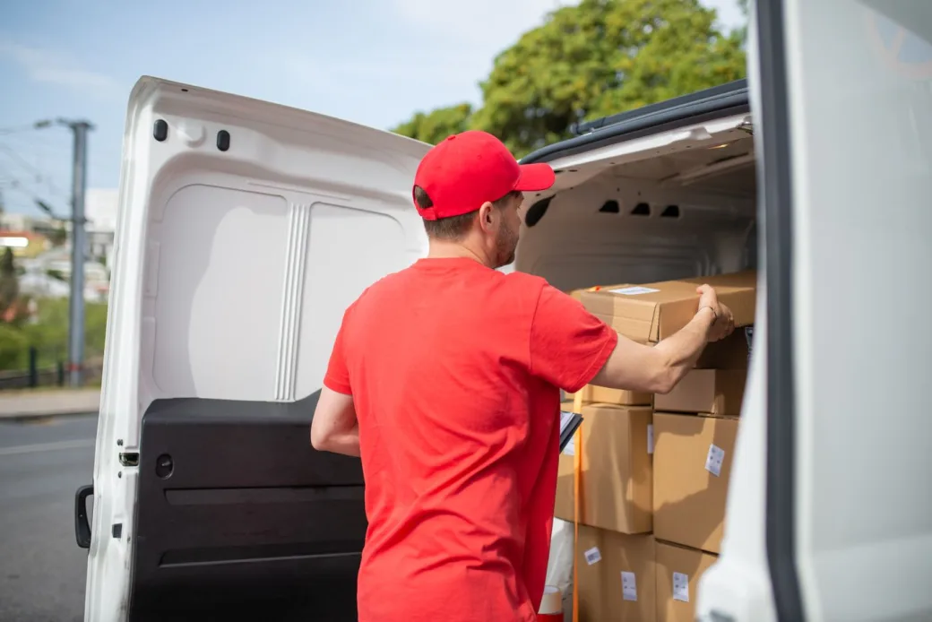 Courier loading stacked cardboard boxes into the back of a delivery van