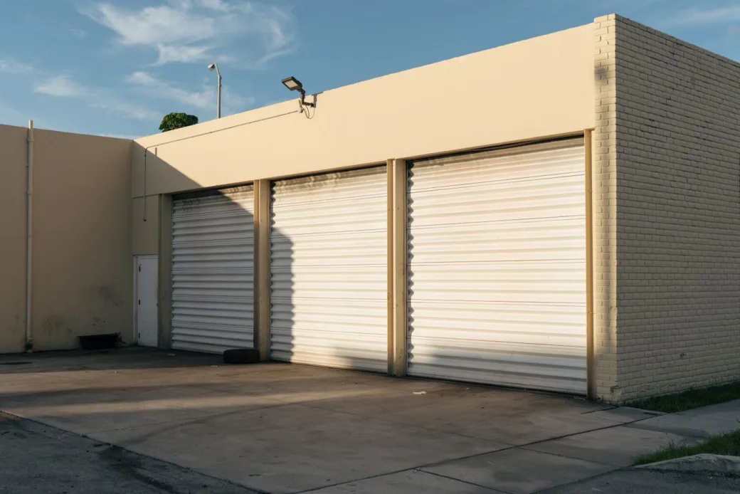 Row of three clean white roll-up storage unit doors on a beige building in warm afternoon light