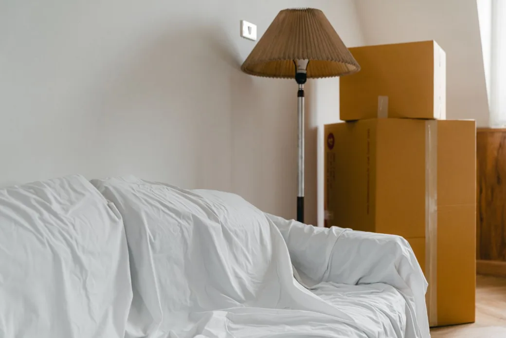 White-covered sofa, floor lamp, and stacked cardboard boxes in a bright room ready for storage